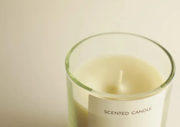 Zoom sur une bougie artisanale parfumée dans un contenant en verre transparent, étiquetée 'SCENTED CANDLE', avec une cire naturelle de couleur crème