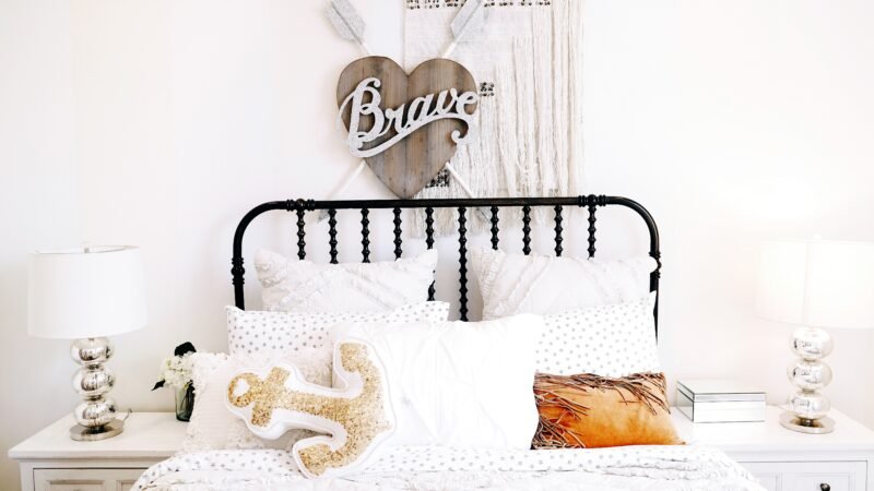Chambre d’enfant tendance minimaliste avec lit en métal noir, déco murale « Brave » et coussins décoratifs bohèmes.
